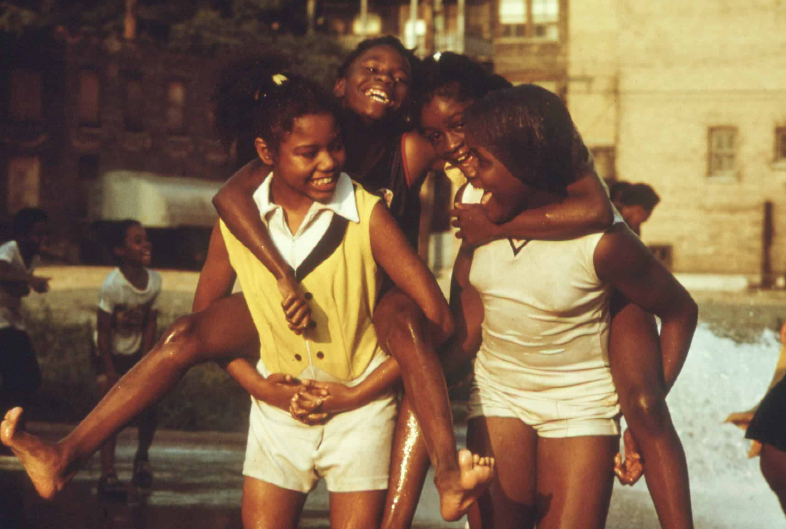 A historical photo of a group of young Black women playing in the street on a summer day